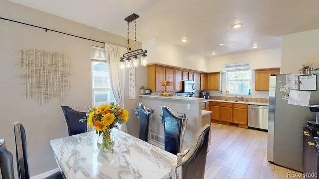 a kitchen with stainless steel appliances kitchen island granite countertop a refrigerator a stove a sink dishwasher a dining table and chairs with wooden floor