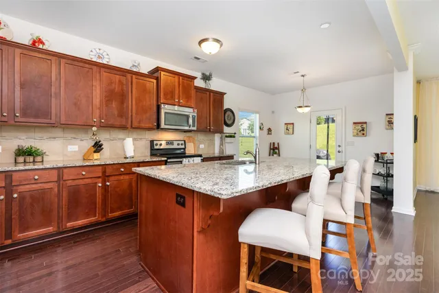 a kitchen with stainless steel appliances granite countertop a table chairs in it and wooden floors
