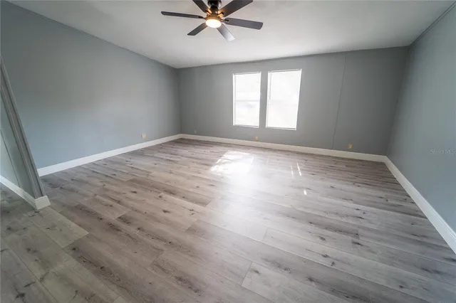 an empty room with wooden floor fan and windows