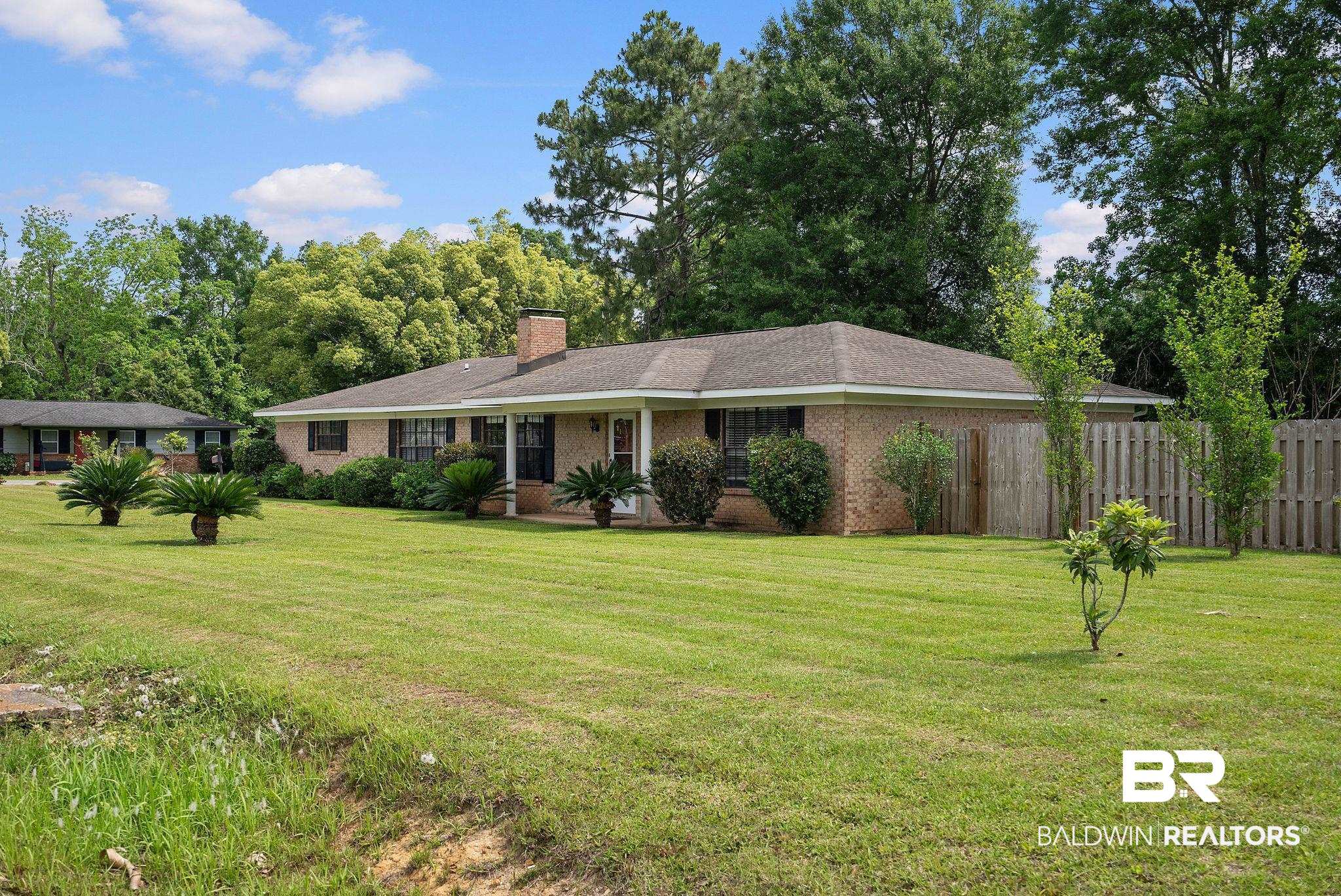 716 North Cedar Street Foley, AL 36535 - Photo 3 of 25 Brick exterior ranch-style home featuring a covered front porch with white columns, a shingle roof, and a prominent brick chimney