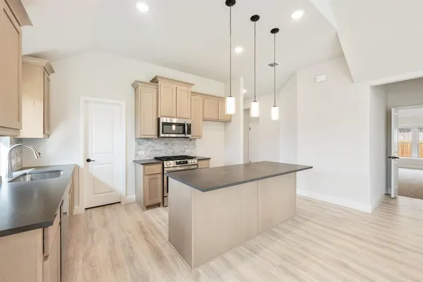 a kitchen with stainless steel appliances granite countertop a stove a sink a refrigerator and a wooden floor