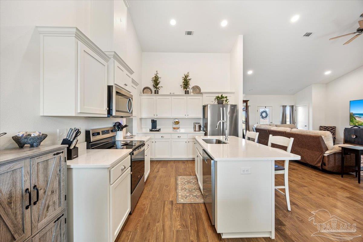 9303 Salter Road Pace, FL 32571 - Photo 6 of 23 a open kitchen with stainless steel appliances kitchen island a stove a sink dishwasher and a refrigerator with wooden floor