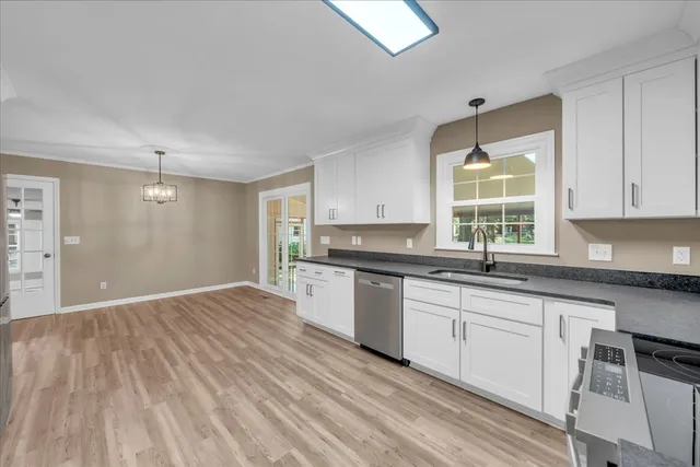 a kitchen with granite countertop a stove a sink and white cabinets with wooden floor