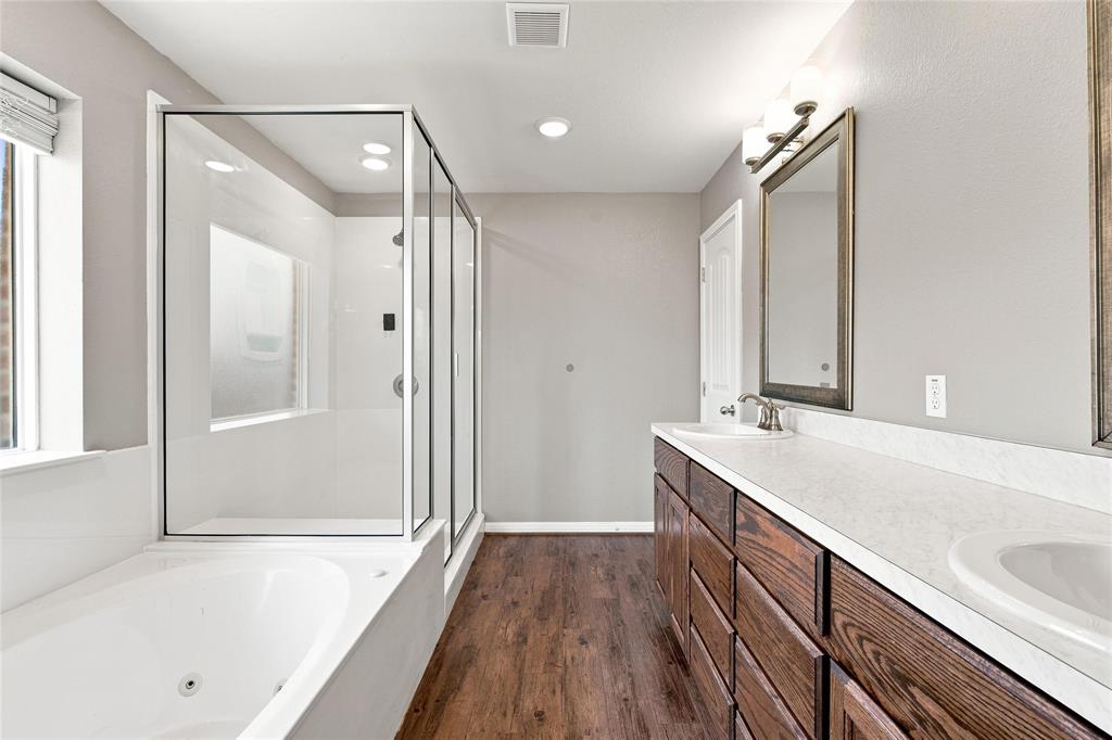 204 Raven Ridge Court Waco, TX 76705 - Photo 9 of 19 Dual vanity with integrated sinks, wood-finish cabinetry, frameless glass shower enclosure, built-in bathtub, and wood-finish flooring