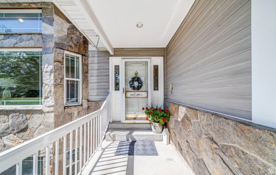 1273 Grayson Court Sandy, UT 84094 - Photo 3 of 27 Stone facade and siding exterior featuring a white paneled entry door with sidelights, overhead recessed lighting, and a white railing system