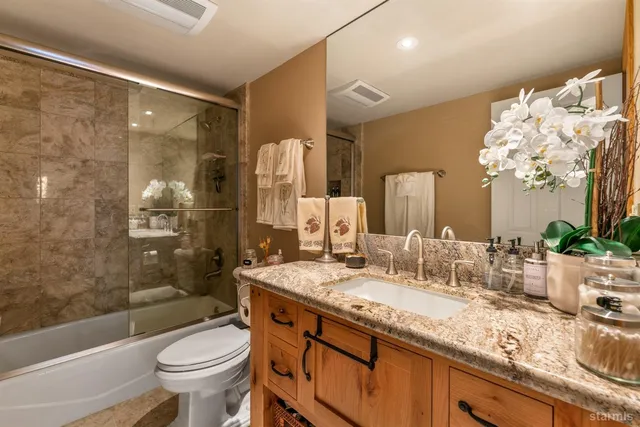 a bathroom with a granite countertop sink a toilet a mirror a bathtub and shower
