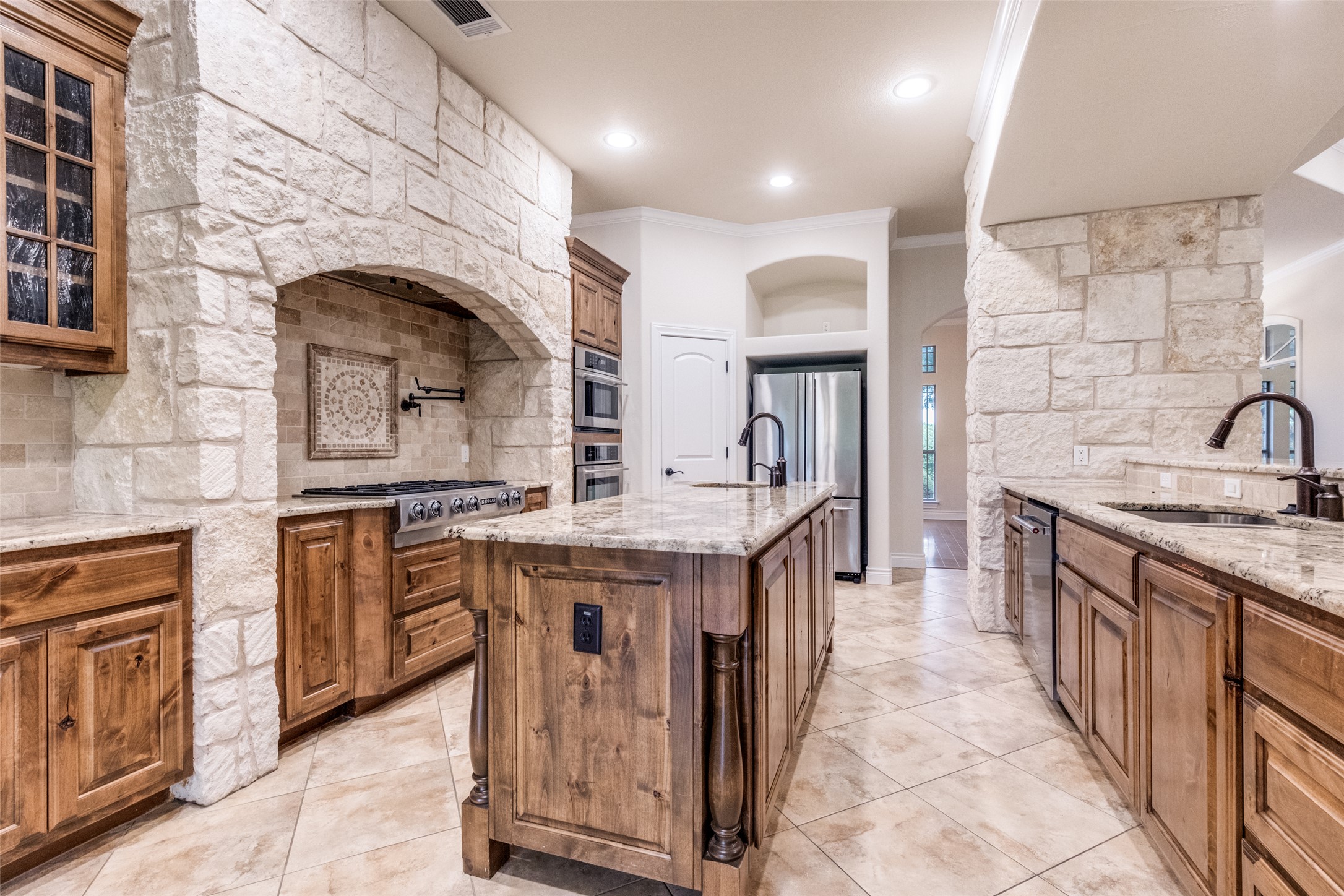 101 Copper Leaf Court Georgetown, TX 78633 - Photo 13 of 31 Kitchen featuring an arched stone range hood, stainless steel gas range, stone-finish tile flooring, granite countertops, and wood cabinetry with multiple storage options