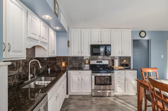 a kitchen with stainless steel appliances granite countertop a stove top oven a sink dishwasher and a refrigerator with wooden cabinets