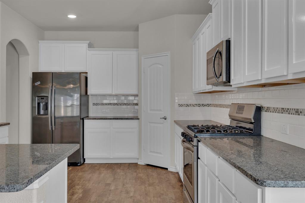 610 Bassett Hall Road Fate, TX 75189 - Photo 9 of 28 Kitchen featuring dark stone countertops, light hardwood / wood-style floors, white cabinets, and appliances with stainless steel finishes