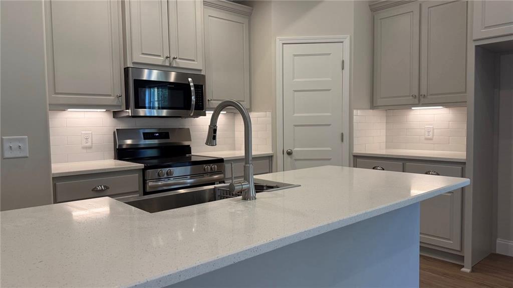 472 Stringer Weeks Road Smiths Station, AL 36877 - Photo 2 of 4 Kitchen featuring stainless steel appliances, decorative backsplash, light stone countertops, and wood finished floors