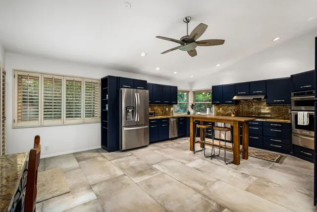 a kitchen with stainless steel appliances kitchen island granite countertop a refrigerator a stove a sink a dining table and chairs with wooden floor