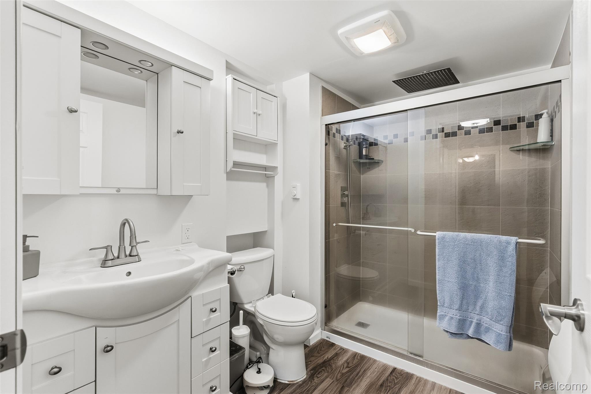 2227 North Graf Road Caro, MI 48723 - Photo 39 of 51 Vanity with integrated sink, white cabinetry with silver hardware, wood-finish flooring, toilet, and glass-enclosed shower with tiled walls