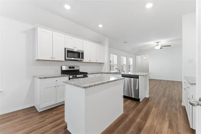 a kitchen with granite countertop a stove top oven a sink dishwasher and a refrigerator with wooden floor