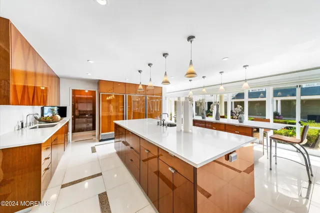 a large kitchen with kitchen island a large counter top space a sink a stove and a view of living room