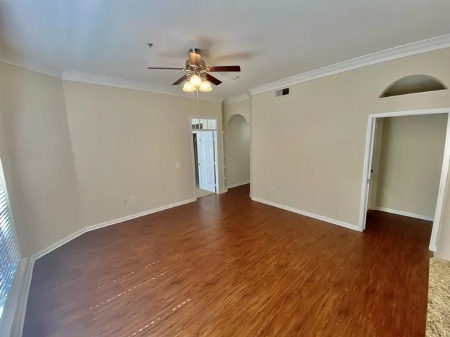 a view of an empty room with wooden floor and a ceiling fan