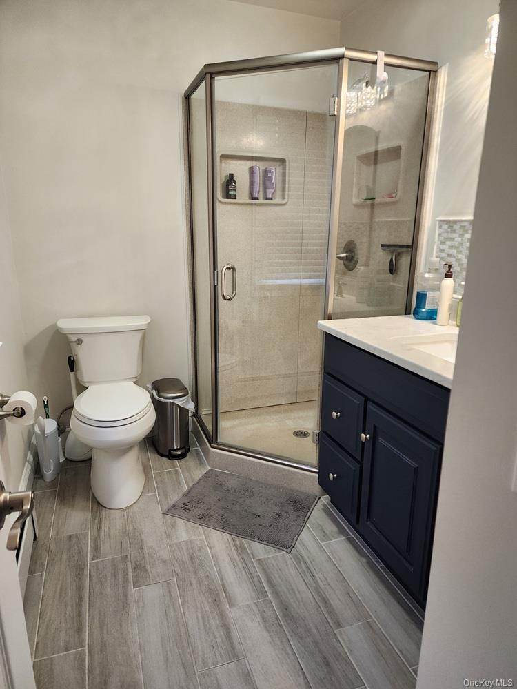 46 Cortlandt Road Mahopac, NY 10541 - Photo 15 of 32 Bathroom featuring a corner glass-enclosed shower with integrated shelving, a dark blue vanity with a white countertop and under mount sink, and wood-finish tile flooring