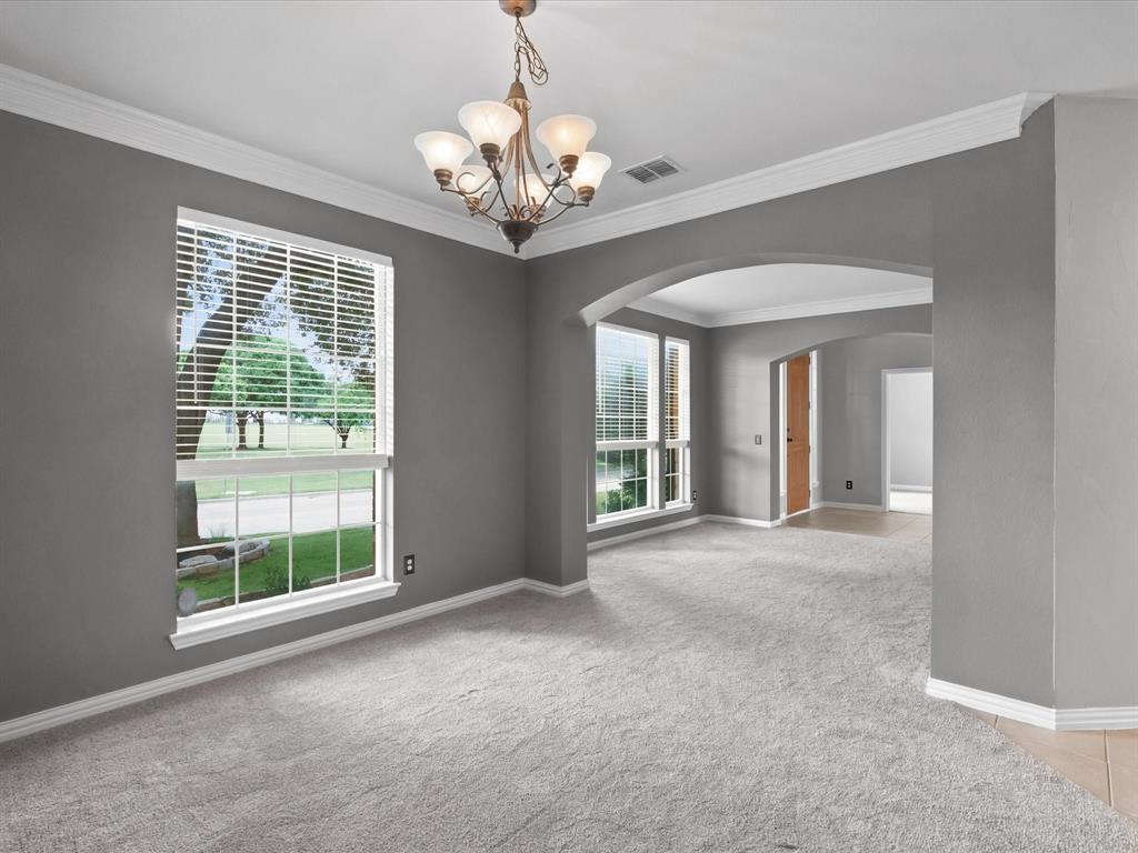 11104 Rogers Road Frisco, TX 75033 - Photo 3 of 37 Spacious room featuring light gray carpet flooring, multiple windows with blinds, a decorative chandelier, crown molding, and an arched entryway