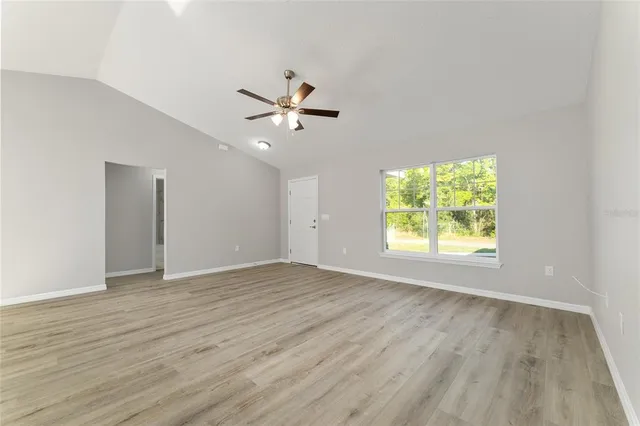 an empty room with wooden floor chandelier fan and windows