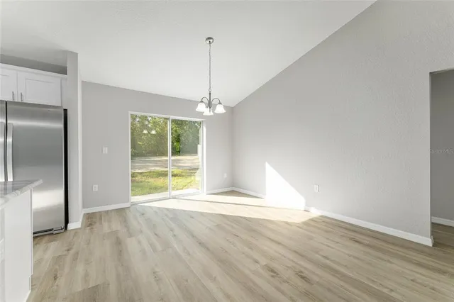 a view of an empty room with wooden floor fridge and a kitchen view