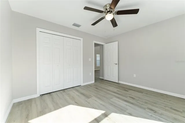 an empty room with wooden floor ceiling fan and windows