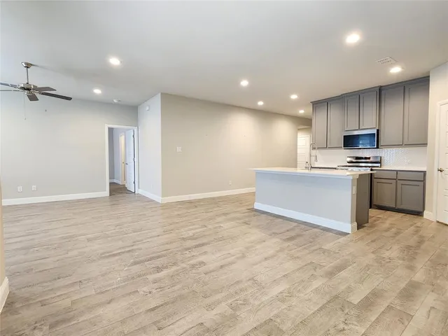 an empty room with wooden floor ceiling fan and windows
