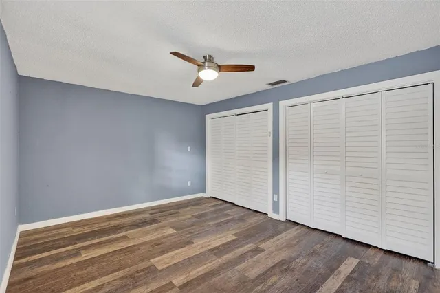 an empty room with wooden floor ceiling fan and windows
