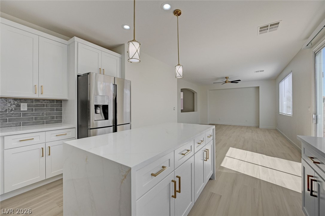 9687 Ridgebluff Avenue Las Vegas, NV 89148 - Photo 14 of 57 Kitchen with stainless steel refrigerator with ice dispenser, hanging light fixtures, white cabinets, decorative backsplash, and a kitchen island