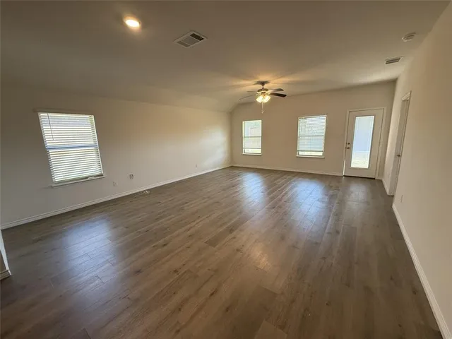 an empty room with wooden floor windows and fan
