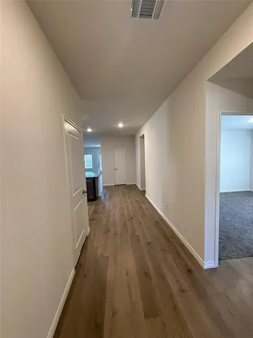 a view of a hallway with wooden floor and a kitchen