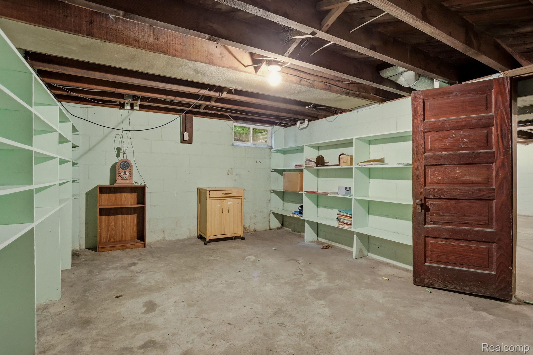 3814 South Towerline Road Bridgeport, MI 48722 - Photo 36 of 52 Basement space featuring extensive built-in shelving, concrete flooring, exposed wood beam ceiling, painted block walls, and a wood-panel interior door