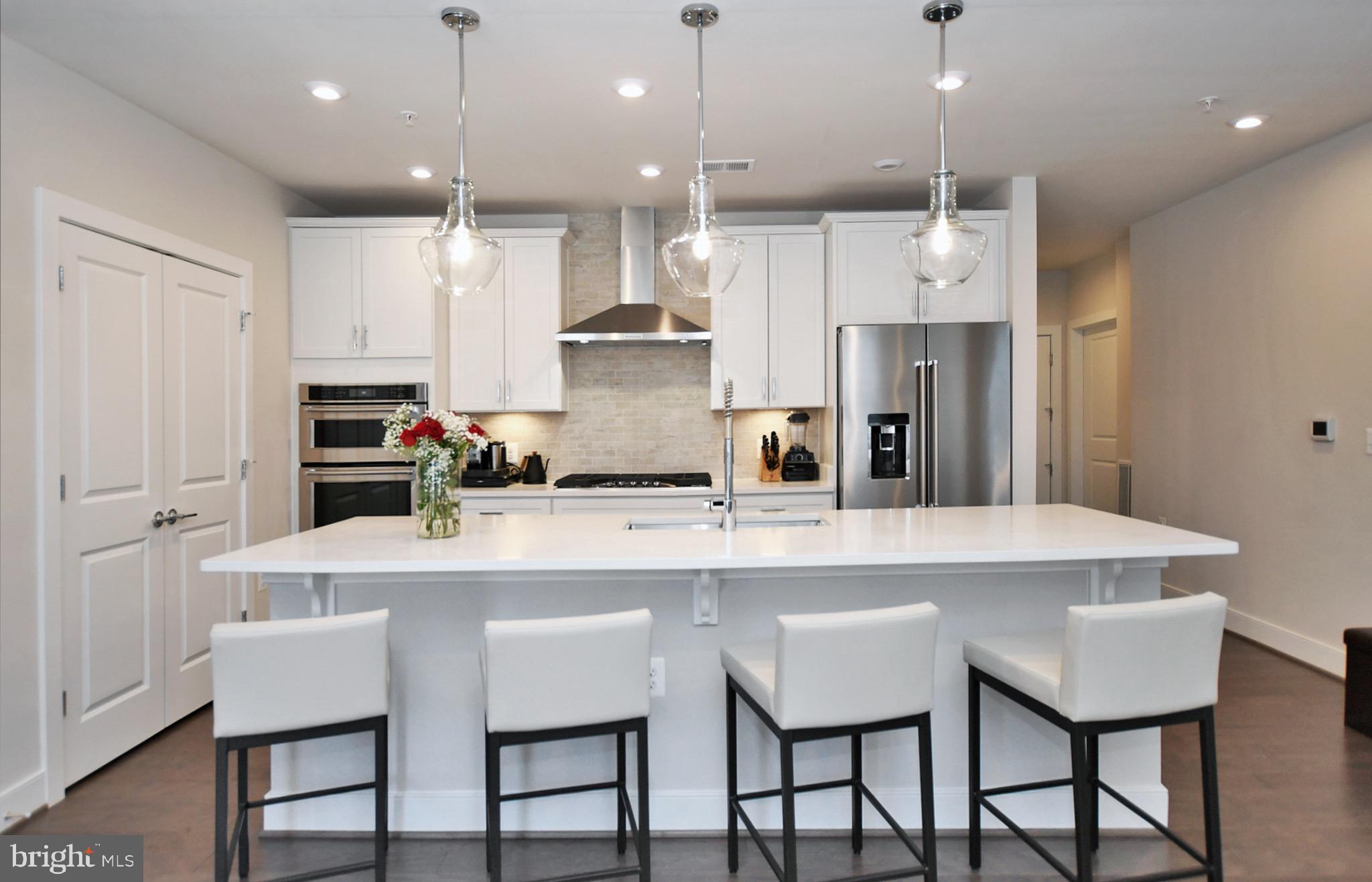 a kitchen with stainless steel appliances granite countertop a dining table chairs refrigerator and white cabinets