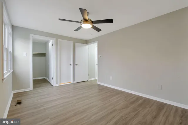 a view of an empty room with wooden floor and a ceiling fan