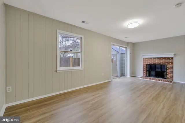a view of an empty room with wooden floor fireplace and a window