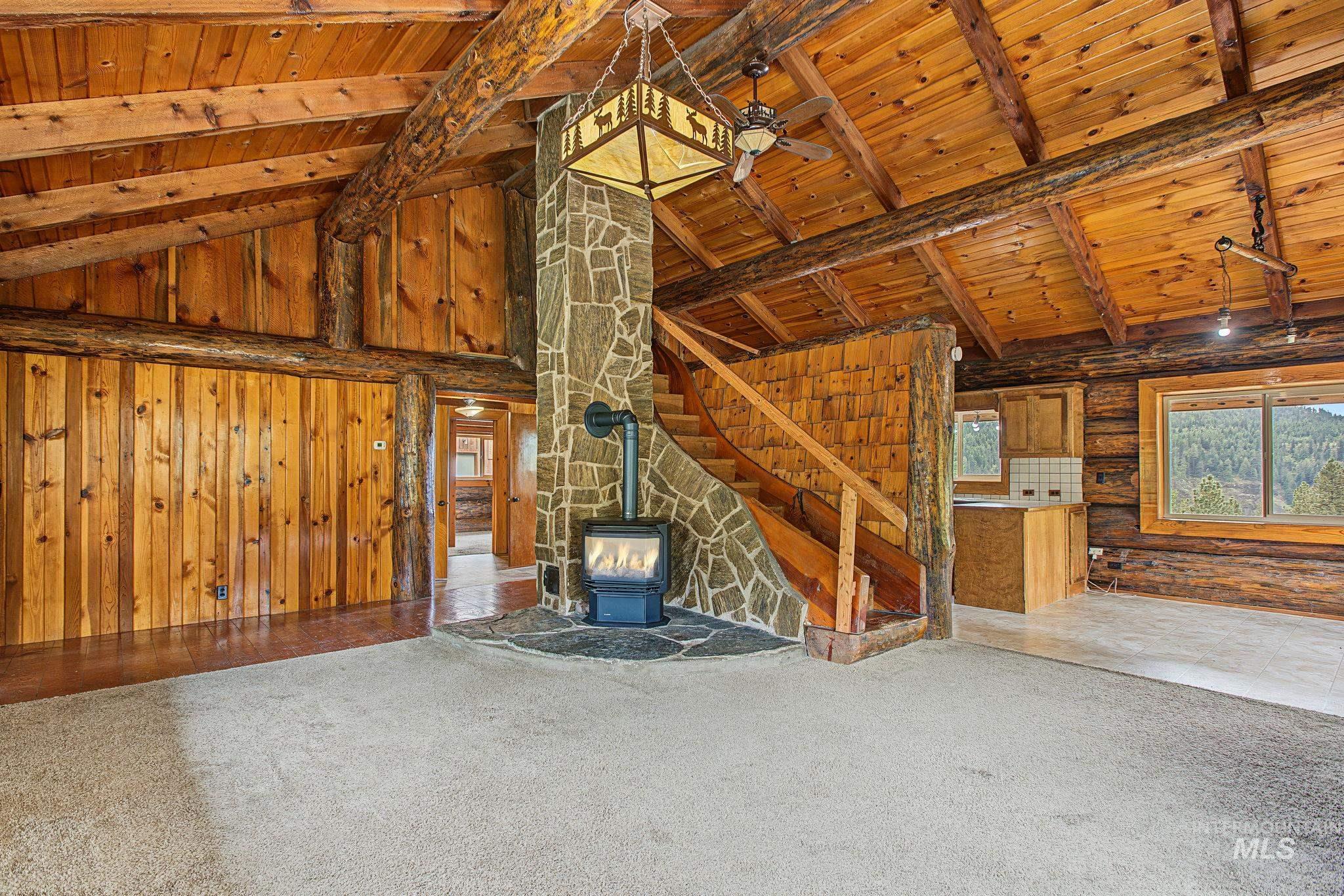 2926 Wells Bench Road Orofino, ID 83544 - Photo 8 of 48 Vaulted wood-paneled ceilings with exposed beams, central stone-clad fireplace with a wood-burning stove, wood-paneled walls, and a wood staircase with a matching railing