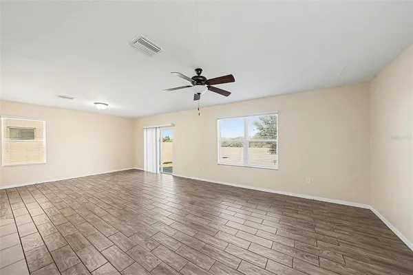 an empty room with wooden floor ceiling fan and windows