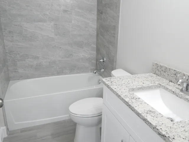 a bathroom with a granite countertop bathtub sink vanity mirror and toilet