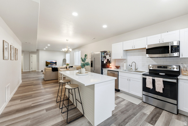 1434 West Stable Street Lindon, UT 84042 - Photo 75 of 76 Kitchen featuring stainless steel appliances, open floor plan, a breakfast bar area, white cabinets, and a kitchen island