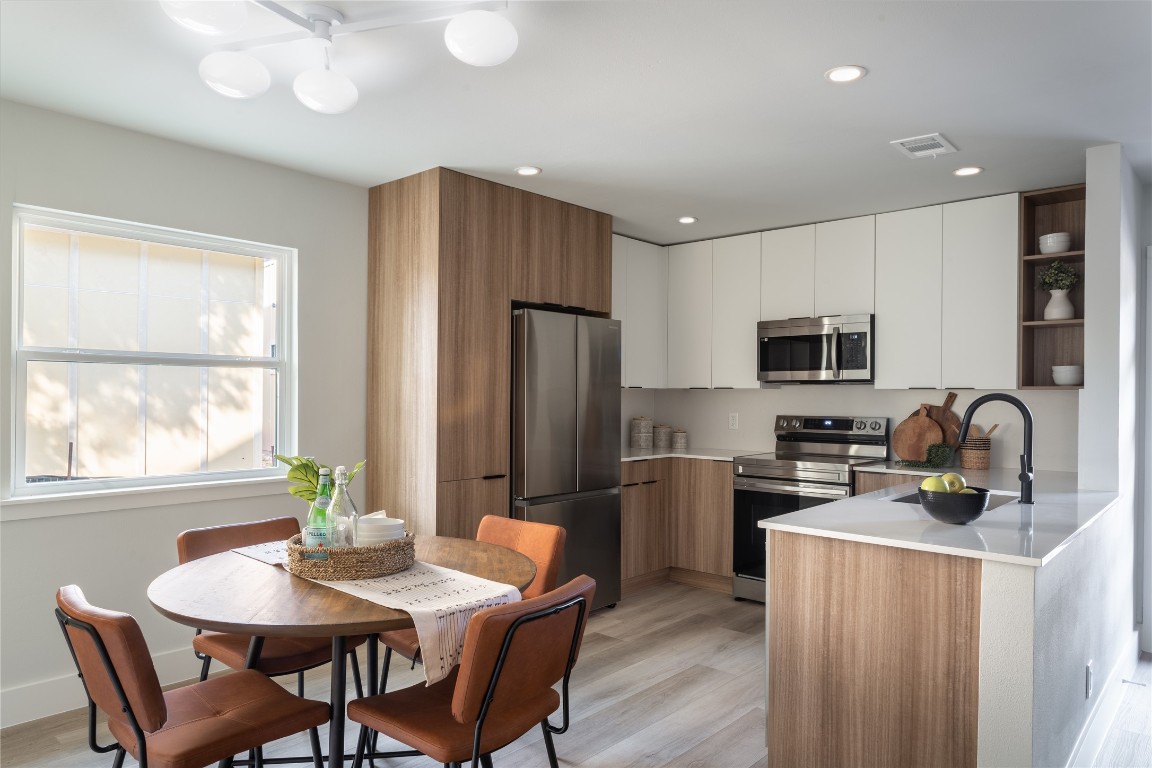 a kitchen with stainless steel appliances granite countertop a refrigerator a stove a sink dishwasher a dining table and chairs with wooden floor