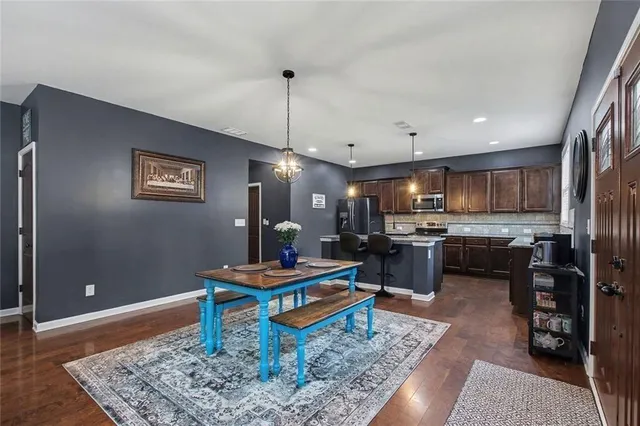 a kitchen with stainless steel appliances granite countertop a refrigerator a stove a sink dishwasher a dining table and chairs with wooden floor