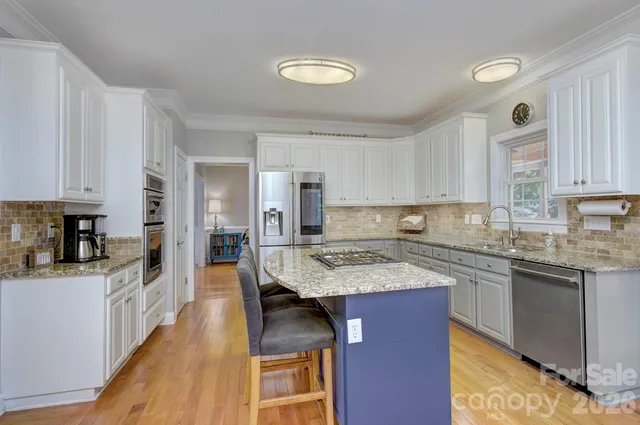 a kitchen with stainless steel appliances granite countertop a stove top oven a sink dishwasher and white cabinets with wooden floor