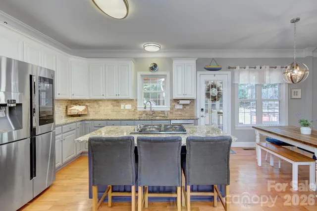 a kitchen with stainless steel appliances granite countertop a stove a refrigerator a sink dishwasher a dining table and chairs with wooden floor