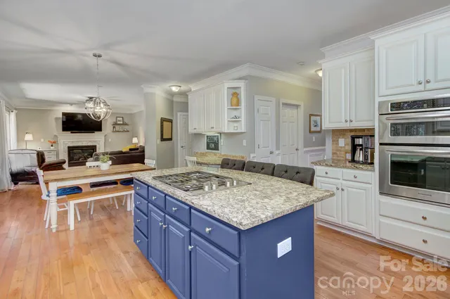 a kitchen with stainless steel appliances granite countertop a stove top oven a sink dishwasher and white cabinets with wooden floor