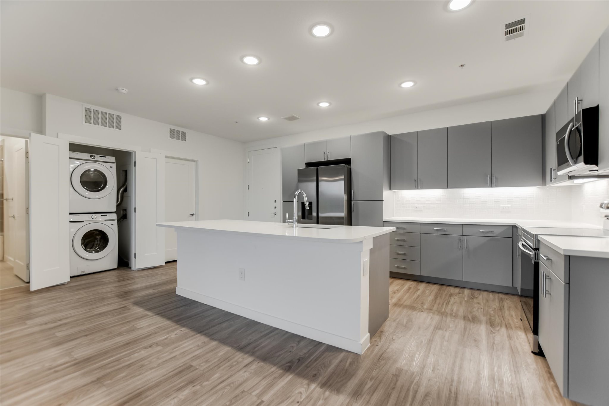 4801 Springdale Road, Unit 1207 Austin, TX 78723 - Photo 2 of 10 Kitchen with gray cabinetry, stainless steel appliances, a kitchen island with sink, stacked washer and dryer, and recessed lighting