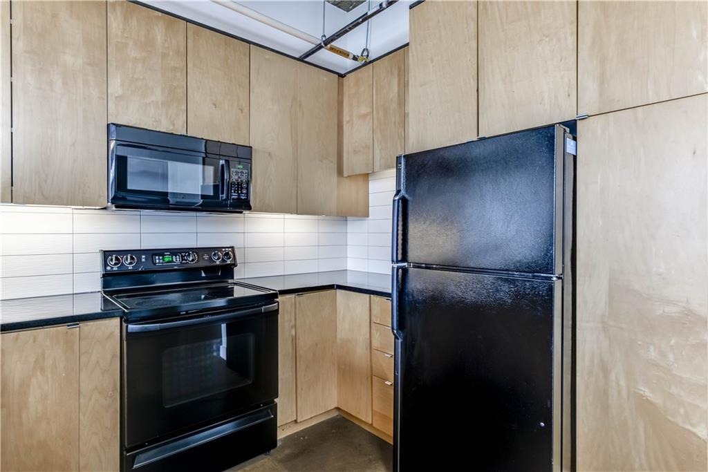 710 Colorado Street, Unit G9 Austin, TX 78701 - Photo 3 of 25 A well-appointed kitchen showcasing contemporary black appliances and sleek wood cabinetry.