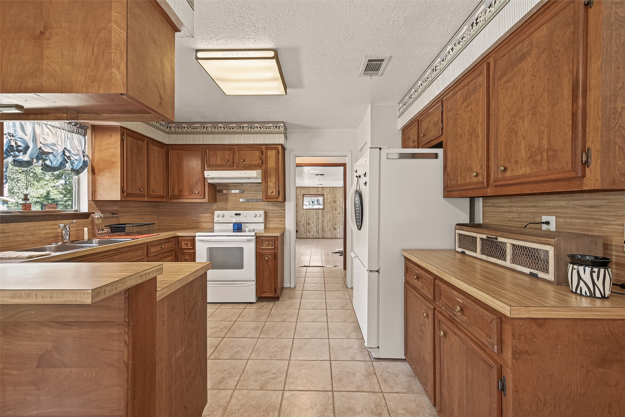 11535 Willis Waukegan Road Conroe, TX 77303 - Photo 19 of 47 This kitchen features warm wood cabinetry, ample counter space, and a classic design. It includes a white stove and refrigerator stay. Natural light from the window and a view of the property make doing dishes more pleasurable.