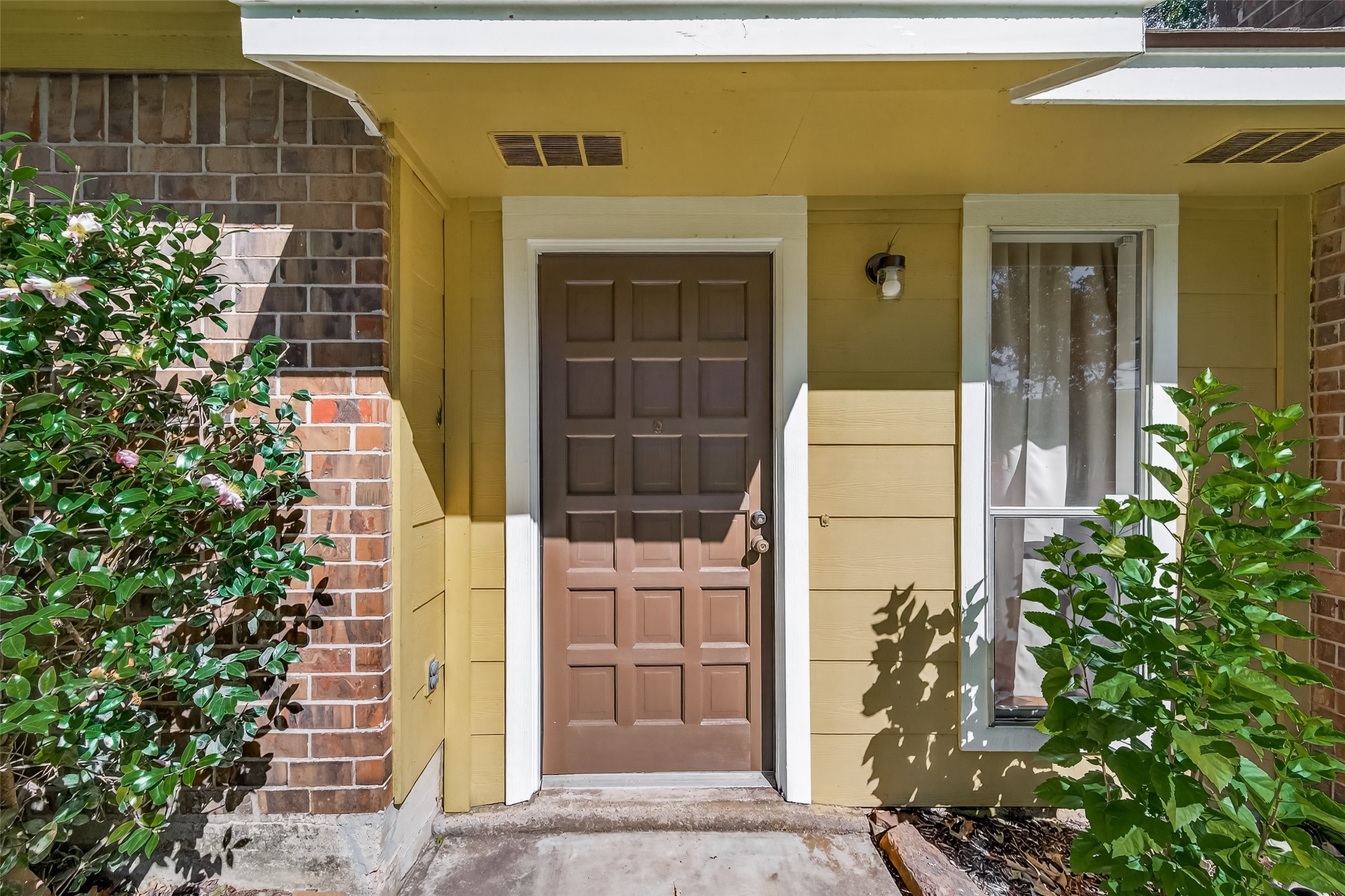 11535 Willis Waukegan Road Conroe, TX 77303 - Photo 4 of 47 Charming front entrance with a brown door, surrounded by brick and yellow siding. The area is accented by greenery, providing a welcoming feel.