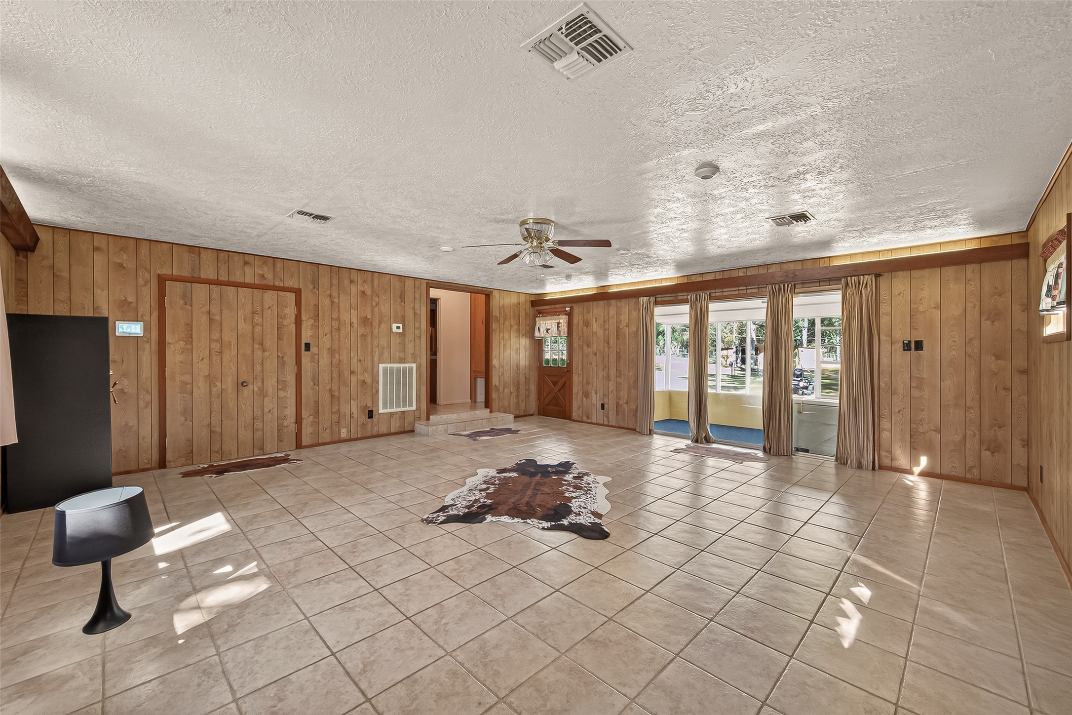 11535 Willis Waukegan Road Conroe, TX 77303 - Photo 8 of 47 Spacious living room with tiled flooring and wood-paneled walls. Features a ceiling fan and large windows/sliding glass door, allowing plenty of natural light. Cozy and inviting space with a rustic touch.
