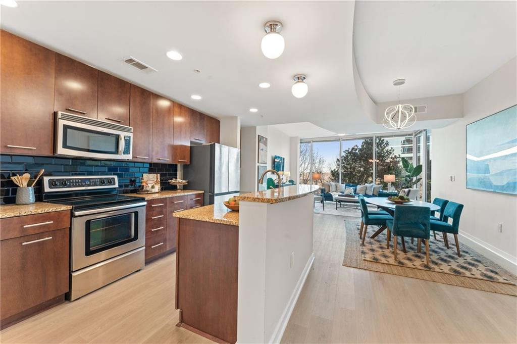 3300 Windy Ridge Parkway Southeast, Unit 809 Atlanta, GA 30339 - Photo 3 of 30 a kitchen with stainless steel appliances kitchen island granite countertop a stove top oven a sink a dining table and chairs with wooden floor