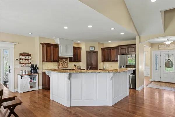 a kitchen with stainless steel appliances granite countertop a stove top oven a sink a refrigerator and white cabinets with wooden floor