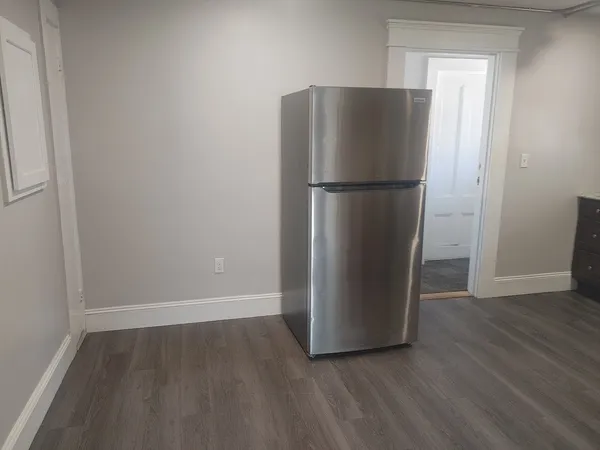 a view of a refrigerator in kitchen and an empty room with wooden floor